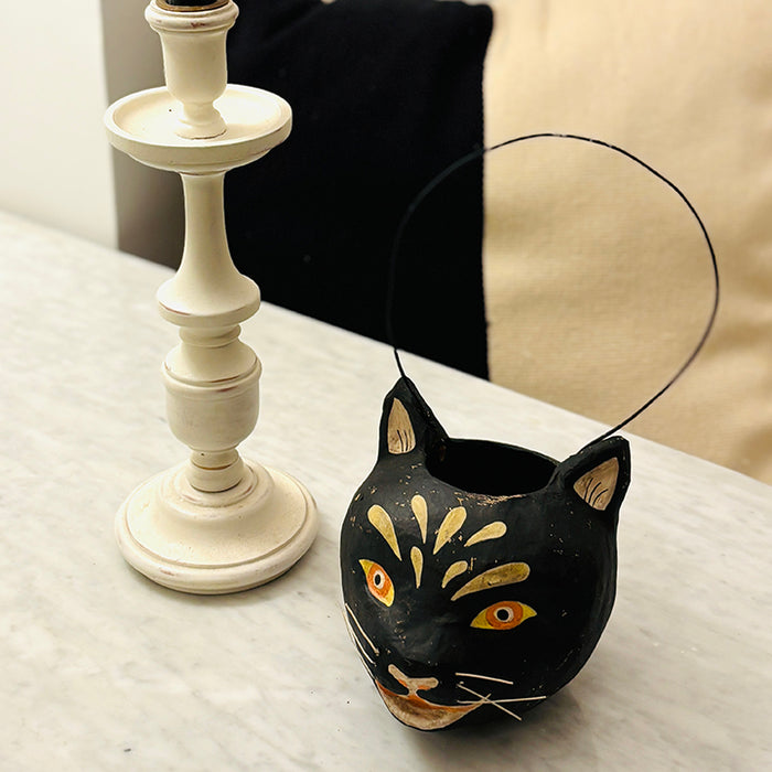 Black cat-shaped Black Cat Papier-Mâché bucket on a surface with a white candlestick in the background.