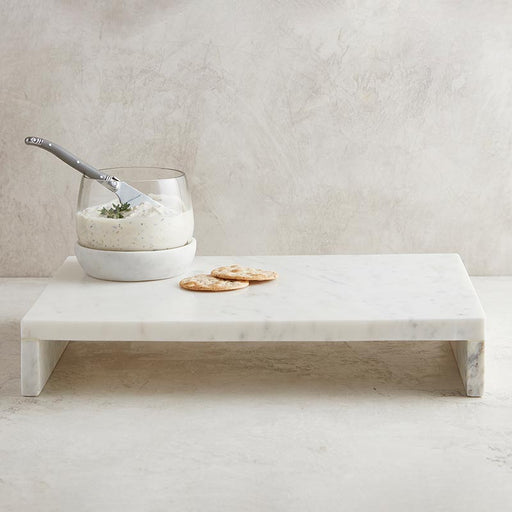 A white marble waterfall stand with a glass bowl and silver serving utensil on top, accompanied by two crackers.