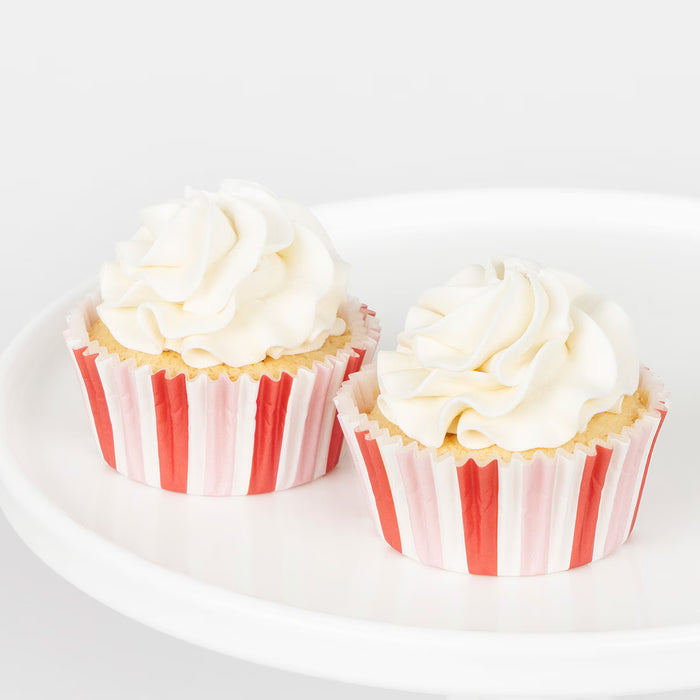 Two cupcakes with white frosting and red and white striped wrappers on a white plate.