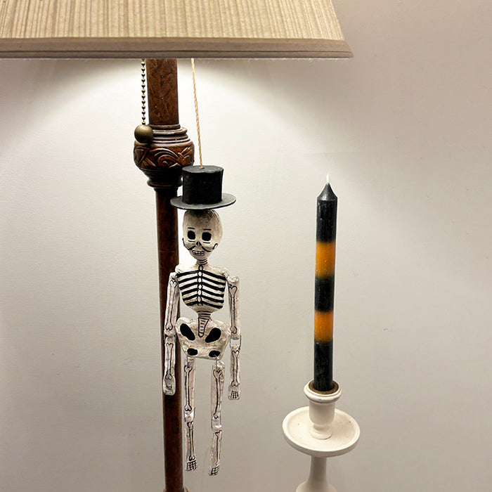 Skeleton figure with a top hat next to a candle on a plain background
