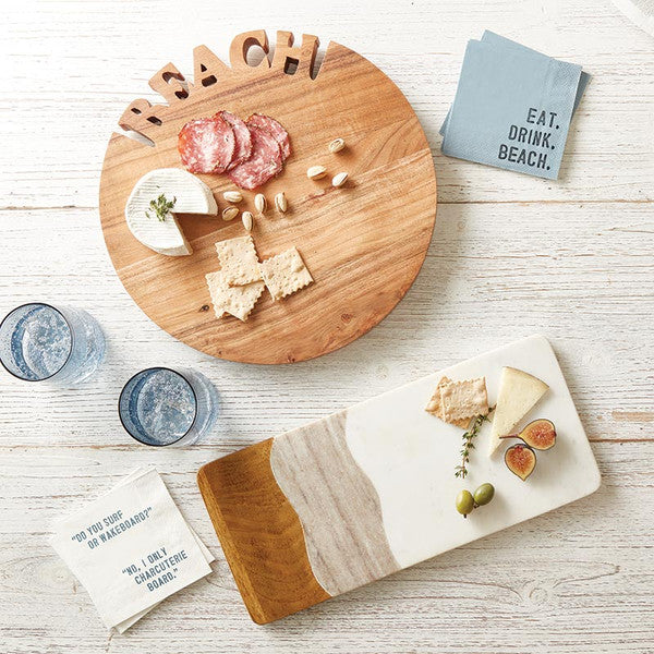 Wooden cutting board with charcuterie and a marble cheese board with figs on a light wooden surface.