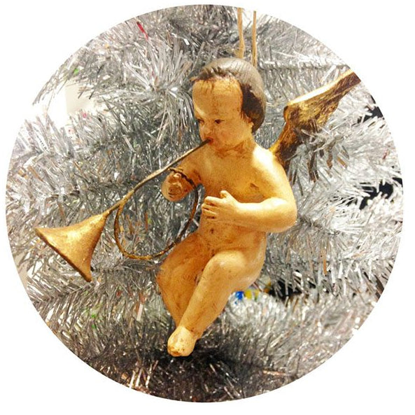 A resin angel ornament with golden wings and a trumpet, set against a silver tinsel background.