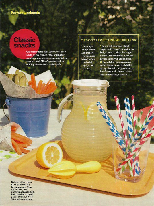 Lemonade pitcher with colorful straws on a wooden cutting board, outdoor setting.