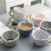 Collection of patterned ceramic cups and bowls on a light surface.