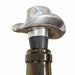 A close-up of a metal wine aerator stopper with a silver cowboy hat design, inserted into the neck of a red wine bottle with a 'PINOT NOIR' label, set against a beige background.