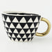 Black and white geometric patterned mug with a gold handle on a white background