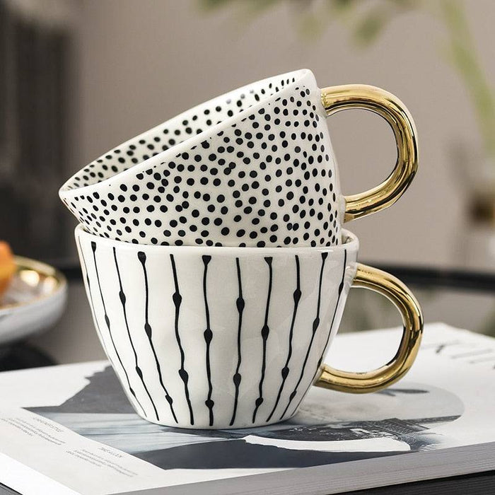 Two ceramic mugs with gold handles stacked on a magazine