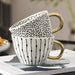 Two ceramic mugs with gold handles stacked on a magazine