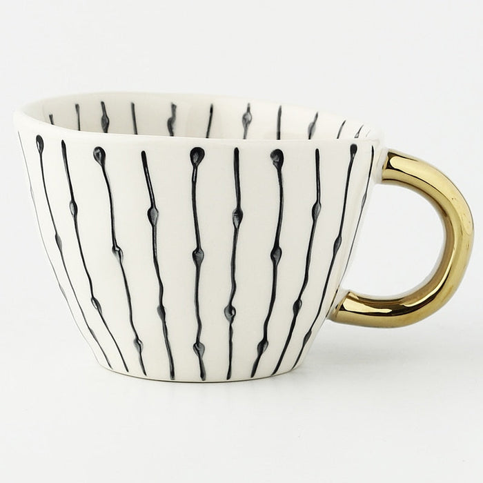 White mug with black abstract patterns and a gold handle on a white background