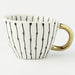 White mug with black abstract patterns and a gold handle on a white background