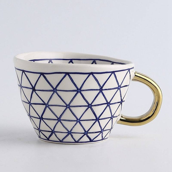 White mug with blue geometric pattern and gold handle on a light gray background