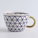 White mug with blue geometric pattern and gold handle on a light gray background