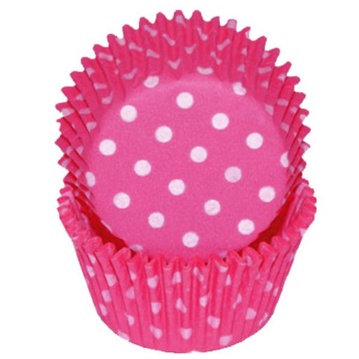 A bright pink standard baking cup with white polka dots