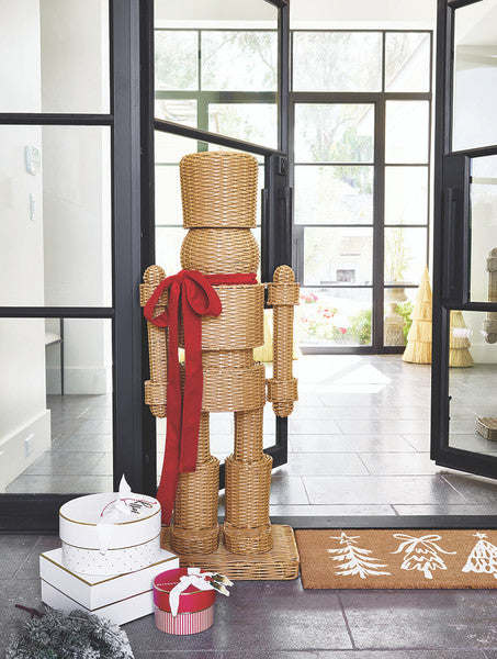 Large all-weather rattan wicker nutcracker with red satin ribbon styled in a home entryway — coastal and preppy Christmas holiday decor for indoor and outdoor display
