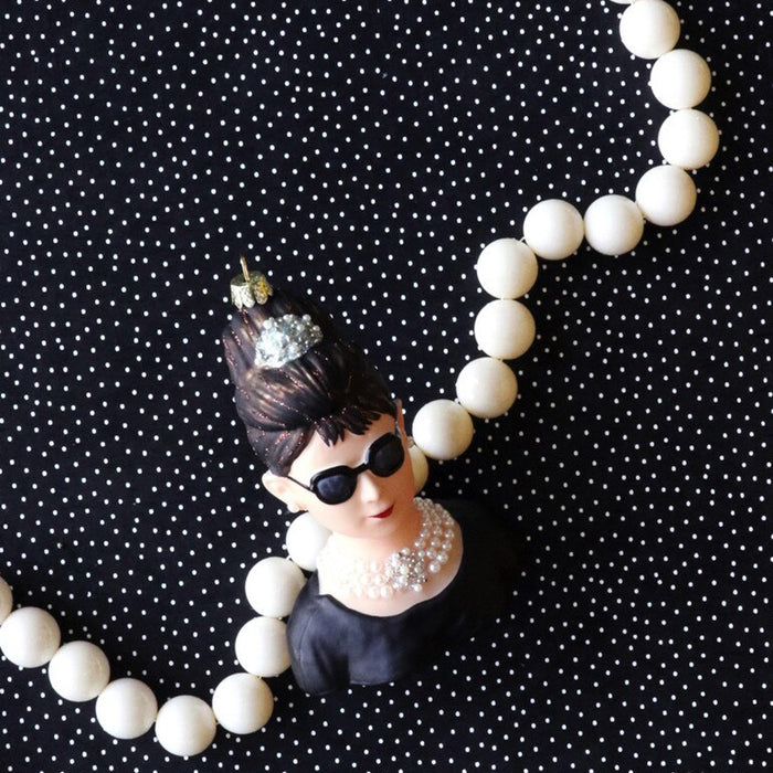 Audrey Hepburn ornament wearing sunglasses and a tiara surrounded by white beads on a black polka dot background.