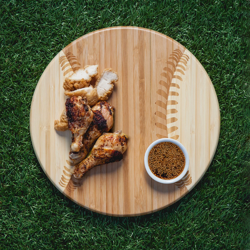 Wooden cutting board with roasted chicken pieces and a bowl of spices on grass