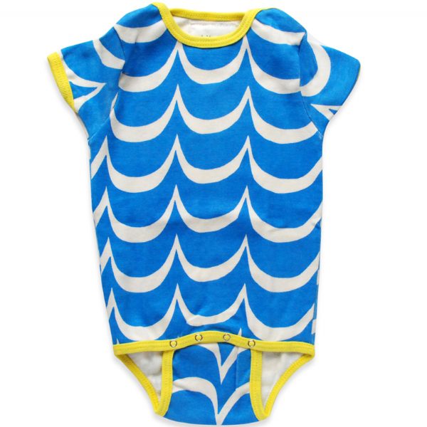 A selection of colorful onesies hanging on a wooden fence, each with a different pattern: one has blue waves, another is pink with hearts, and the last one is yellow with circles.