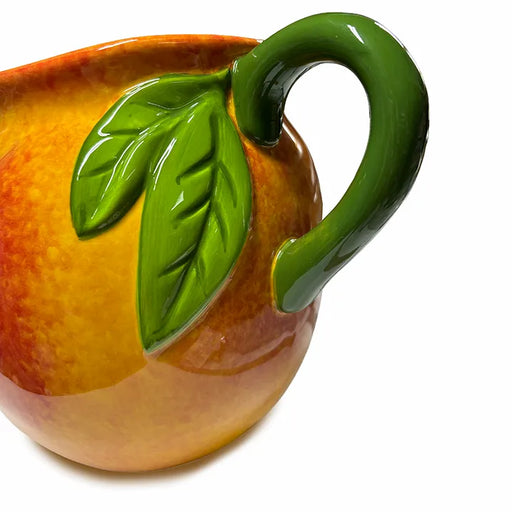 Ceramic pitcher shaped like a peach with a green handle and leaves on a white background