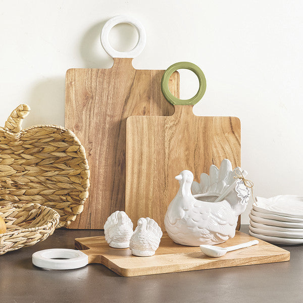 White ceramic turkey gravy boat with spoon and small turkey salt and pepper shakers — an elegant Thanksgiving table serving set styled with wooden cutting boards and woven accents