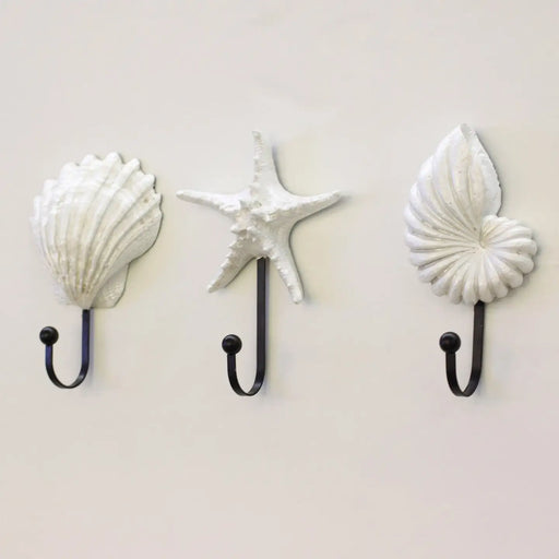 Three wall hooks shaped like shells and a starfish on a light gray background