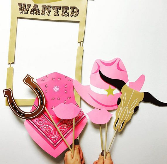 A collection of photo props including a 'Wanted' sign, pistols, a sheriff badge, lips, a cowgirl hat, a pink bandana, a horse ring, and a bull skull, all in pink and designed for photo opportunities.