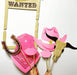 A collection of photo props including a 'Wanted' sign, pistols, a sheriff badge, lips, a cowgirl hat, a pink bandana, a horse ring, and a bull skull, all in pink and designed for photo opportunities.