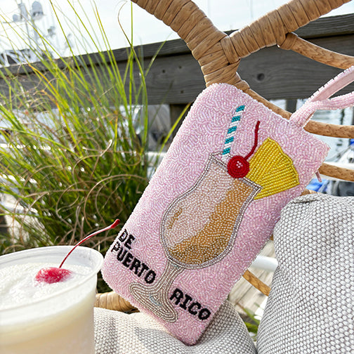 Pink beaded "De Puerto Rico" clutch with piña colada cocktail design styled outdoors at the beach — a fun Puerto Rican souvenir and tropical vacation accessory