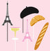 A set of props including a black beret, a pink Eiffel Tower, a yellow champagne glass, a croissant, and a long bread stick, meant for fashion photo shoots with a Paris theme.