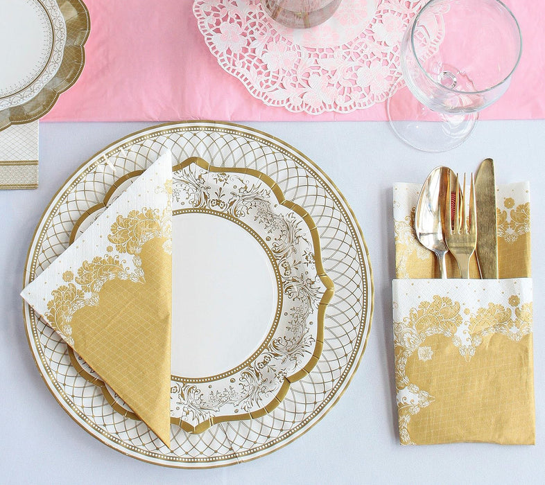 Elegant table setting with gold and white paper plates, napkins, and cutlery on a pink tablecloth.