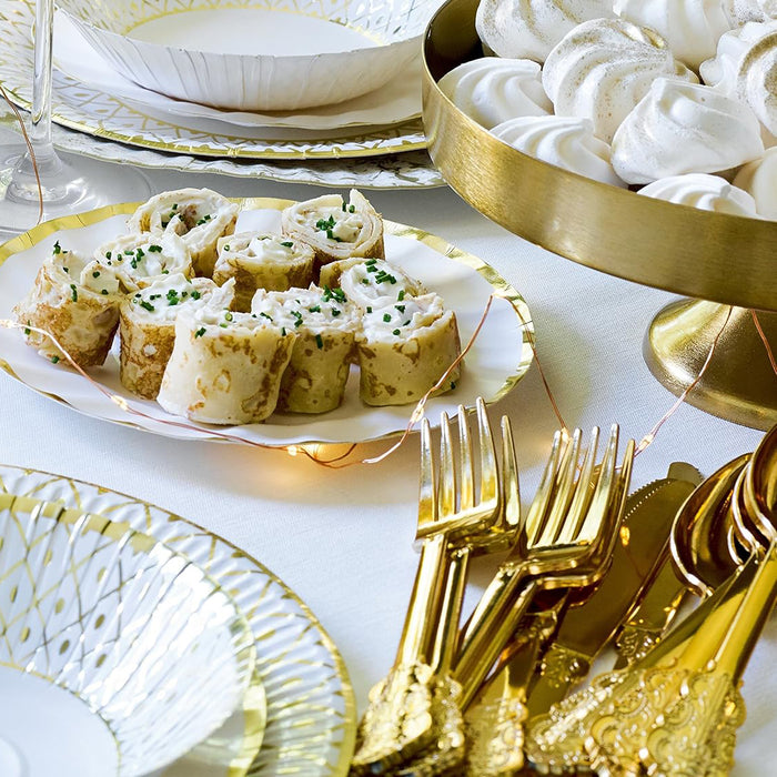 Decorative table setting with gold and white plates, silverware, and a cake stand with white meringues.