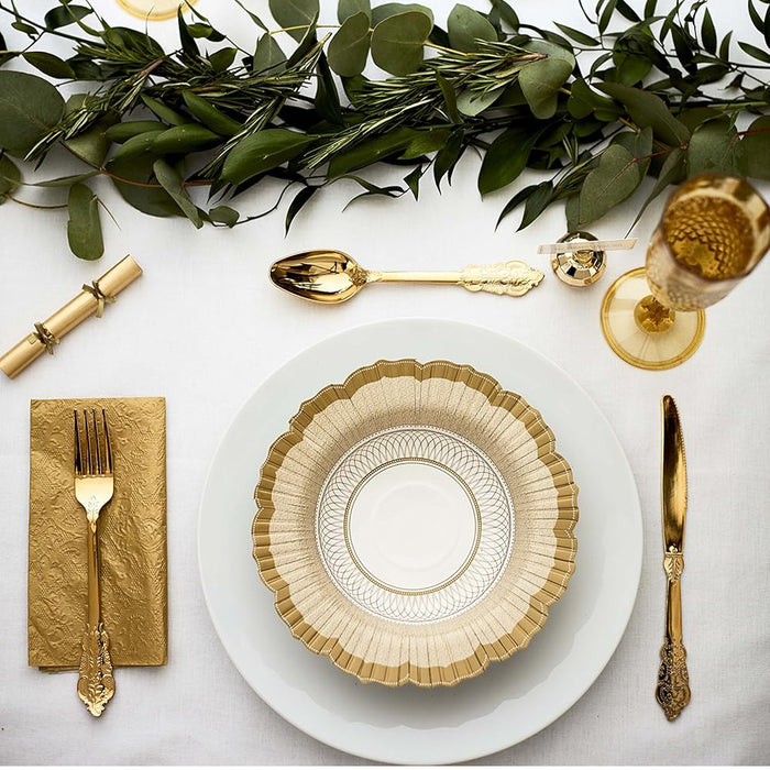 Elegant table setting with gold plates, cutlery, and napkin on a white surface with greenery.