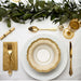 Elegant table setting with gold plates, cutlery, and napkin on a white surface with greenery.