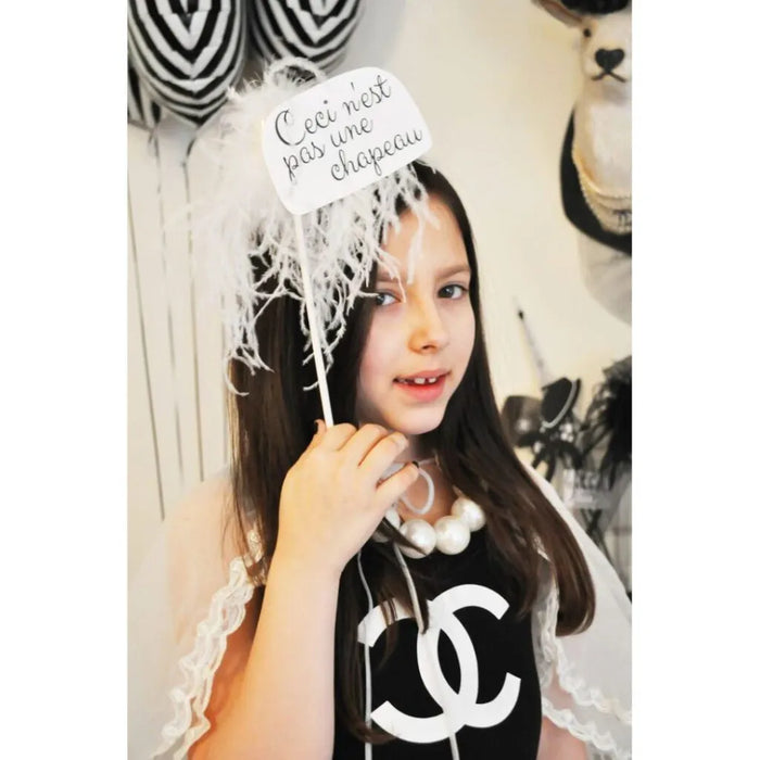 Fashion girl wearing a black dress holding a white hat photo prop with French text.