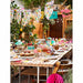 Outdoor table setting with food, drinks, and colorful decorations in a garden.