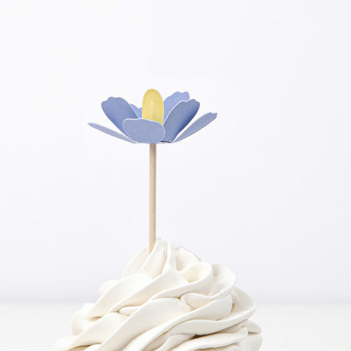 Decorative flower on a stick with a yellow center on top of a white dessert.