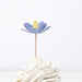 Decorative flower on a stick with a yellow center on top of a white dessert.