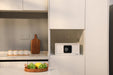 Small safe integrated into a kitchen cabinet with a cutting board and fruit basket on a counter.