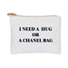 A white canvas zipper pouch with the text 'I NEED A HUG OR A PARIS BAG' printed in black. It features a gold metal zipper with a metal pull.