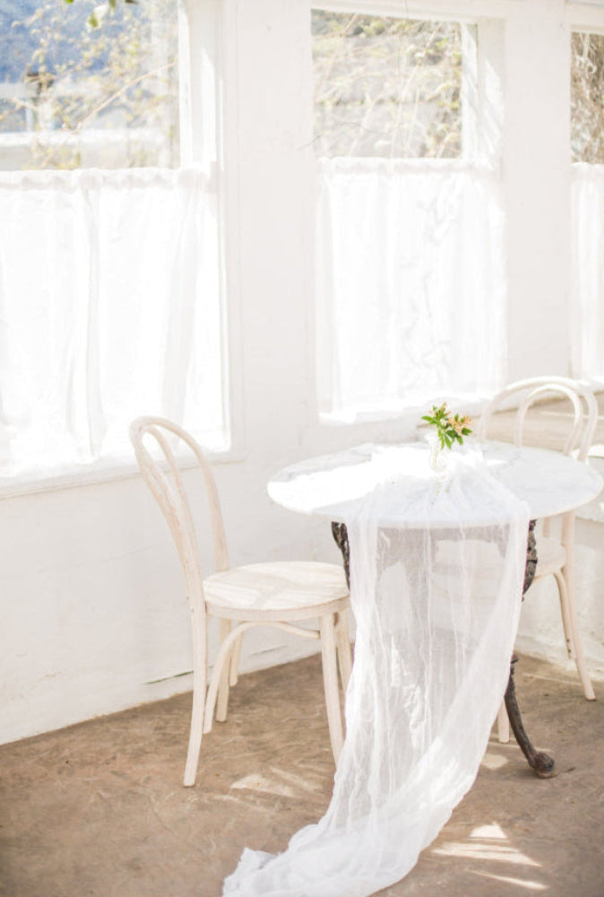 White tablecloth draped over a round table with chairs in a bright room.