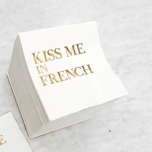 White cocktail napkin with gold foil Kiss Me in French lettering for weddings or Paris theme celebrations