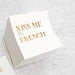 White cocktail napkin with gold foil Kiss Me in French lettering for weddings or Paris theme celebrations