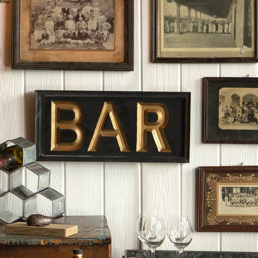 Decorative wall with framed pictures and a gold 'BAR' sign.