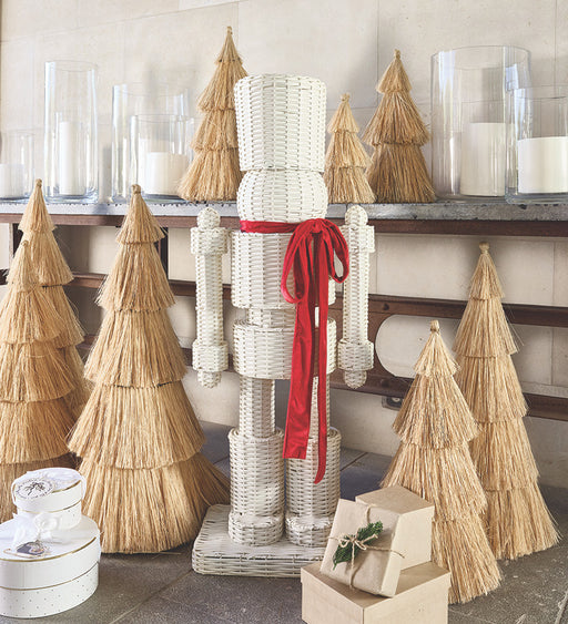 Decorative wicker nutcracker with straw Christmas trees and candles on a shelf.