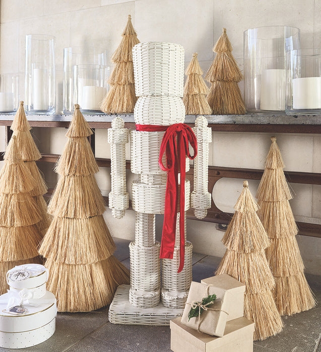 Decorative wicker nutcracker with straw Christmas trees and candles on a shelf.