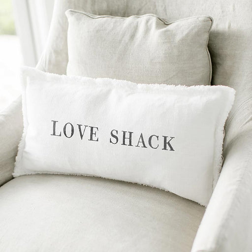 White lumbar pillowcase with the words “Love Shack” in black lettering styled on a neutral chair