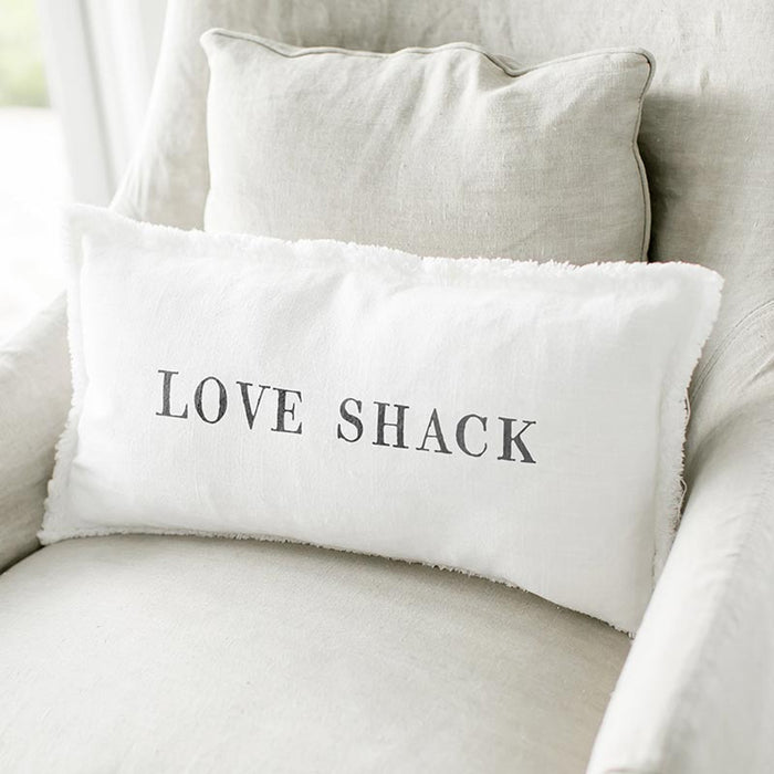 White lumbar pillowcase with the words “Love Shack” in black lettering styled on a neutral chair