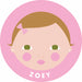 A stylized cartoon baby face illustration inside a pink circle, with the name 'ZOEY' printed at the bottom. The face has light peach skin, brown hair, green eyes, pink cheeks, and a small pink bow.