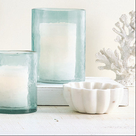 Three glass candle holders with candles on a white surface, with a light blue tint.