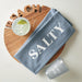 Blue towel with 'Salty' text on a wooden board with a margarita and 'Beach Bum' cup. Wooden round sign with 'BEACH' cut out of the top. Handcrafted acacia wood tray with ‘BEACH’ lettering, styled with summer appetizers and coastal table accessories.