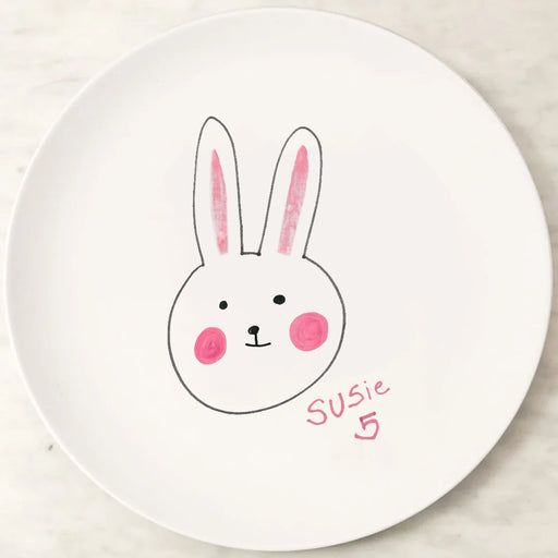 White kids melamine plate with a hand-drawn rabbit face and the name 'Susie' on a light wooden surface.